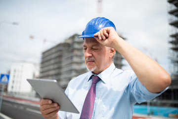 Senior engineer man in suit and helmet working on tablet pc