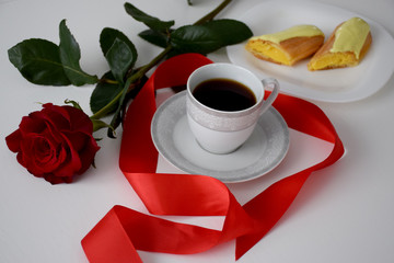 Red rose, red stripe, eclair on white plate, cup of coffee on plate, gray tea set on white table