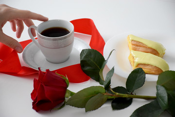 Hand touch, red rose, red stripe, eclair on white plate, cup of coffee on plate, gray tea set on white table