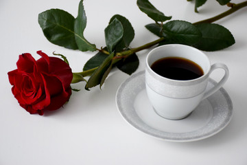 Red rose, cup of coffee on plate, gray tea set on white table