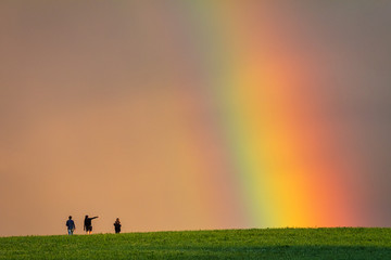 Obraz na płótnie Canvas Landscape right after a rain, colorful rainbow over a grassy meadow with young peoples on a walk.