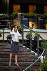 Young mixed-race female talking on mobile standing on the steps of the business center.