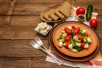 Fresh salad from tomato, cucumber and baby mozzarella. Sunny lunch with crusty bread