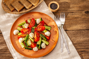 Fresh salad from tomato, cucumber and baby mozzarella. Sunny lunch with crusty bread