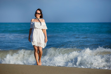 Fototapeta na wymiar Woman in white dress walking on the beach during summer vacation