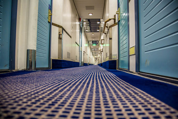 A long corridor in blue style with cabin doors on the deck of a modern passenger ferry