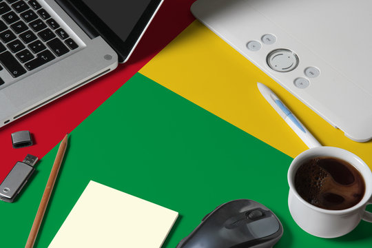 Guinea national flag on top view work space of creative designer with laptop, computer keyboard, usb drive, graphic tablet, coffee cup, mouse on wooden table. - Powered by Adobe