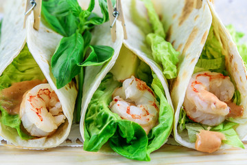 Tacos or wraps with fresh green and shrimps with sauce closeup. Fast food concept.
