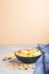 Millet porridge with candied fruits and almonds in blue ceramic bowl on a gray and orange background. Side view, selective focus, copy space.