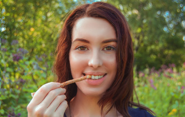 Beautiful young girl with brown hair cleans her  healthy white teeth with eco miswak stick. Smiling woman uses  organic toothbrush at nature. Traditional  islamic\arabian  teeth care with siwak.