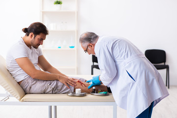 Fototapeta premium Leg injured man visiting old doctor in first aid concept