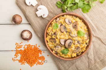 Lentils porridge with champignons. and coriander in a wooden bowl on a white wooden background. Top view, close up.