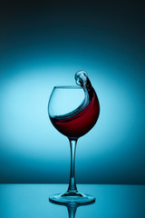 Glass with a splash of red wine on blue background. Splashing red wine in a glass