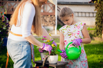 Woman gardener helping her daughter to pour garden flower pot.