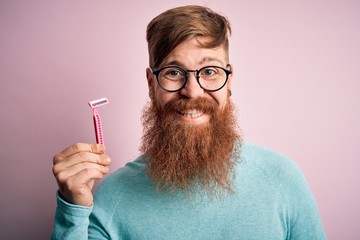 Redhead Irish man with beard holding beauty razor for shaving and skin care over pink background...