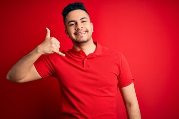 Naklejka premium Young handsome man wearing red casual polo standing over isolated background smiling doing phone gesture with hand and fingers like talking on the telephone. Communicating concepts.