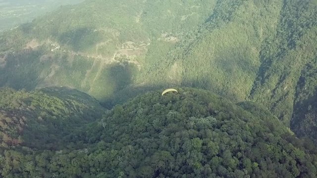 drone shot from rear and above a yellow paragliding flying over the beautiful mountains of jarabacoa dominican republic