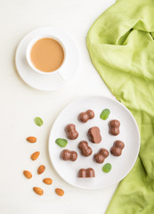 Chocolate candies with almonds and a cup of coffee on a white wooden background. top view.