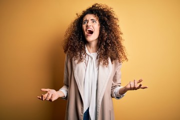 Young beautiful brunette woman with curly hair and piercing wearing casual t-shirt and diadem crazy and mad shouting and yelling with aggressive expression and arms raised. Frustration concept.