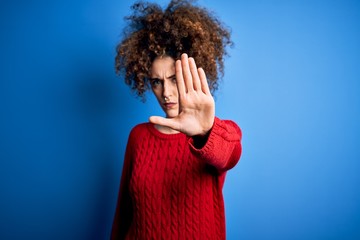 Young beautiful woman with curly hair and piercing wearing casual red sweater doing stop sing with...