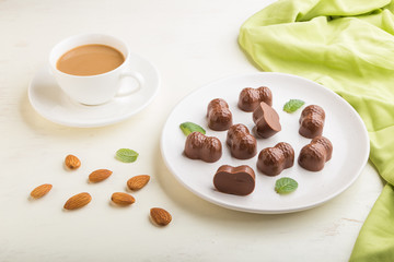 Chocolate candies with almonds and a cup of coffee on a white wooden background. side view.