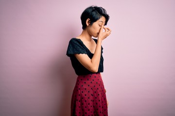 Young beautiful asian girl wearing casual dress standing over isolated pink background tired rubbing nose and eyes feeling fatigue and headache. Stress and frustration concept.