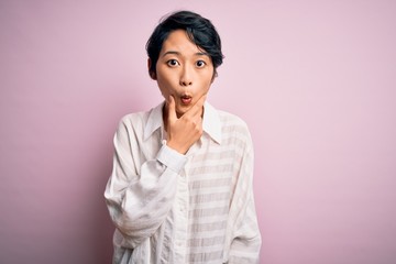 Young beautiful asian girl wearing casual shirt standing over isolated pink background Looking fascinated with disbelief, surprise and amazed expression with hands on chin