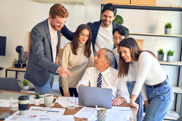 Group of business workers smiling happy and confident. One of them sitting and partners standing around. Working together with smile on face looking at the laptop at the office