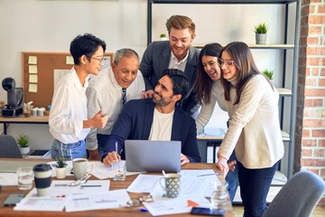 Group of business workers smiling happy and confident. One of them sitting and partners standing around. Working together with smile on face looking at the laptop at the office