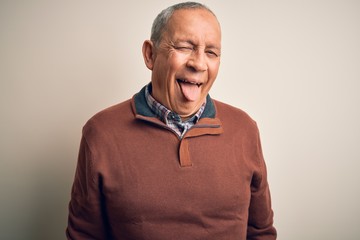 Senior handsome man  wearing elegant sweater standing over isolated white background sticking tongue out happy with funny expression. Emotion concept.