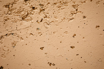 The texture of the concrete wall with irregularities, cracks, potholes, painted in sand color. Abstract background.