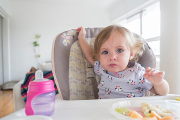 Little cute girl eating alone in her chair.