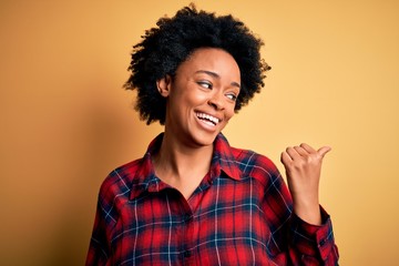 Fototapeta na wymiar Young beautiful African American afro woman with curly hair wearing casual shirt smiling with happy face looking and pointing to the side with thumb up.