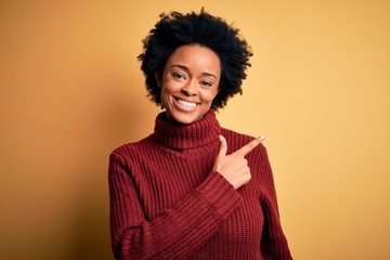 Obraz na płótnie Canvas Young beautiful African American afro woman with curly hair wearing casual turtleneck sweater cheerful with a smile on face pointing with hand and finger up to the side with happy and natural