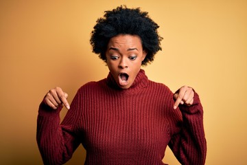 Fototapeta na wymiar Young beautiful African American afro woman with curly hair wearing casual turtleneck sweater Pointing down with fingers showing advertisement, surprised face and open mouth