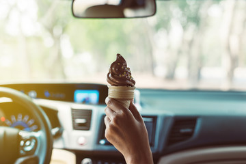 Woman hands holding chocolate ice cream waffle cone calories in car at light green nature background - obrazy, fototapety, plakaty