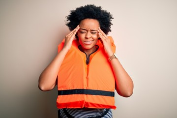 Young African American afro woman with curly hair wearing orange protection lifejacket with hand on head for pain in head because stress. Suffering migraine.