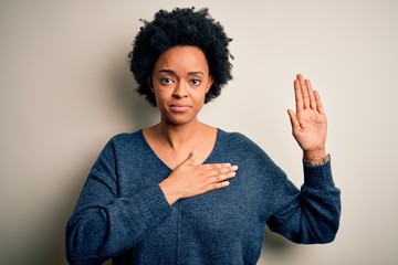 Young beautiful African American afro woman with curly hair wearing casual sweater Swearing with hand on chest and open palm, making a loyalty promise oath