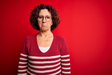 Middle age beautiful curly hair woman wearing casual striped sweater over red background depressed and worry for distress, crying angry and afraid. Sad expression.