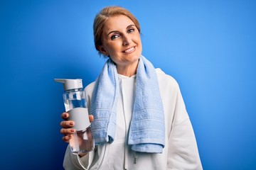Middle age beautiful blonde sportswoman wearing towel holding bottle of water to refreshment with a happy face standing and smiling with a confident smile showing teeth