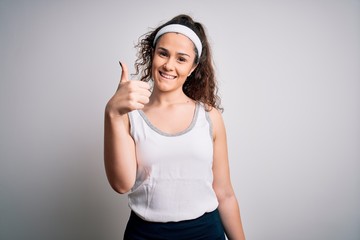 Beautiful sportswoman with curly hair wearing sportswear over isolated white background doing happy thumbs up gesture with hand. Approving expression looking at the camera showing success.