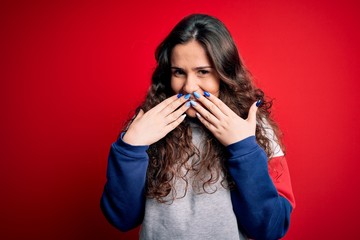 Young beautiful woman with curly hair wearing casual sweatshirt over isolated red background...