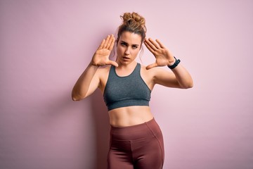 Young beautiful blonde sportswoman doing sport wearing sportswear over pink background doing frame using hands palms and fingers, camera perspective