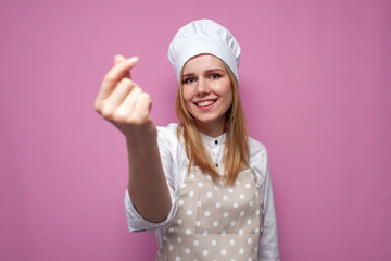 cheerful girl cook in kitchen clothes shows italian heart sign and smiles on a colored background, woman housewife makes hand gesture