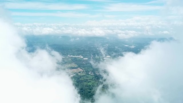 drone footage flying slow above a mass of white clouds bracking through in a cloudy day and showing part of the view of jarabacoa town dominican republic