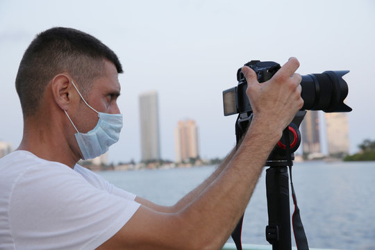 photographer or videographer with a digital camera and a monopod and a protective mask on his face at work takes a panorama of the city