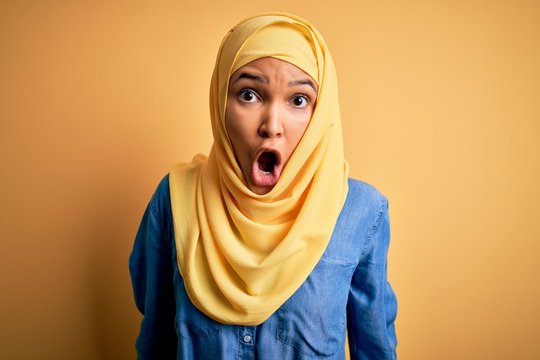 Young Beautiful Woman With Curly Hair Wearing Arab Traditional Hijab Over Yellow Background Afraid And Shocked With Surprise And Amazed Expression, Fear And Excited Face.