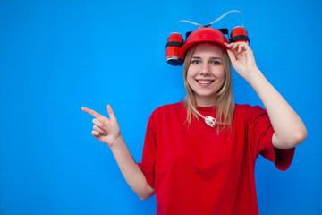 happy funny girl fan in red uniform shows fingers on a place for text and smiles, joyful cheerleader on a blue background