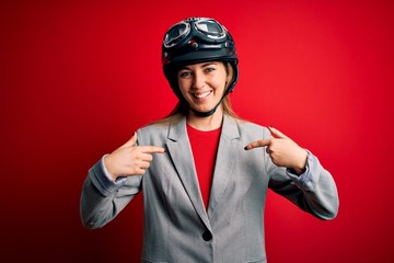 Young beautiful blonde motorcyclist woman wearing motorcycle helmet over red background looking confident with smile on face, pointing oneself with fingers proud and happy.