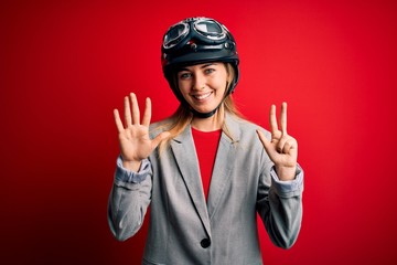Young beautiful blonde motorcyclist woman wearing motorcycle helmet over red background showing and pointing up with fingers number eight while smiling confident and happy.